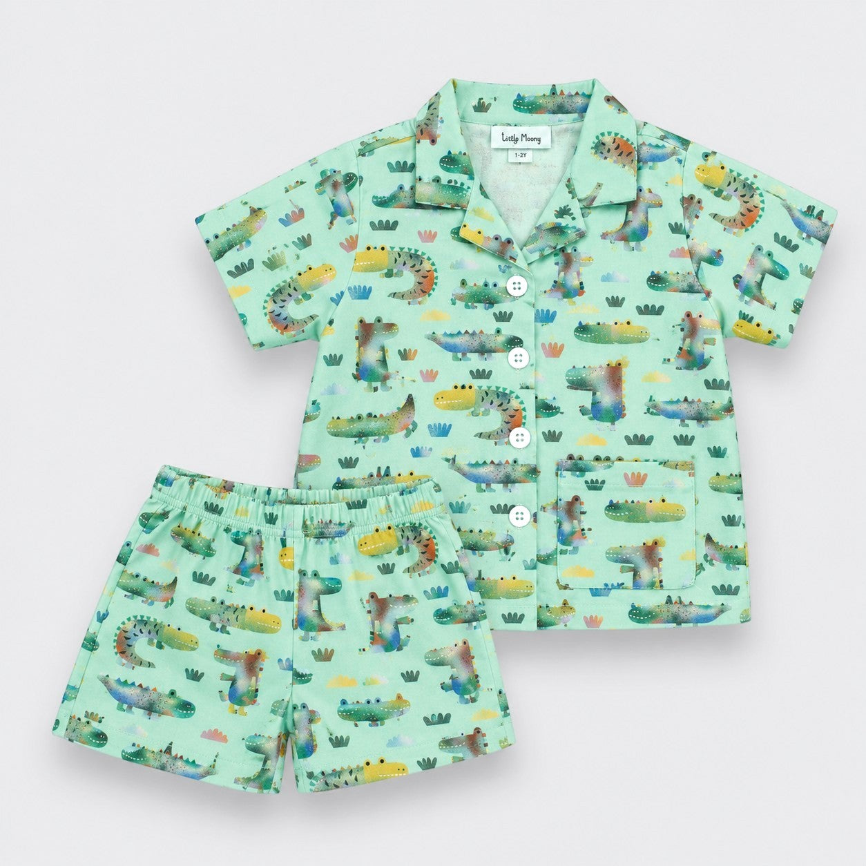 A two-piece alligator set featuring a short-sleeve button-up shirt and matching shorts in a light mint green color with a colorful all-over dinosaur print, displayed on a light gray background.