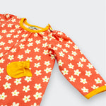 Little Moony Close-up of daisy floral baby romper showing marigold ruffled chest pocket and contrast ribbed cuff on coral interlock knit fabric