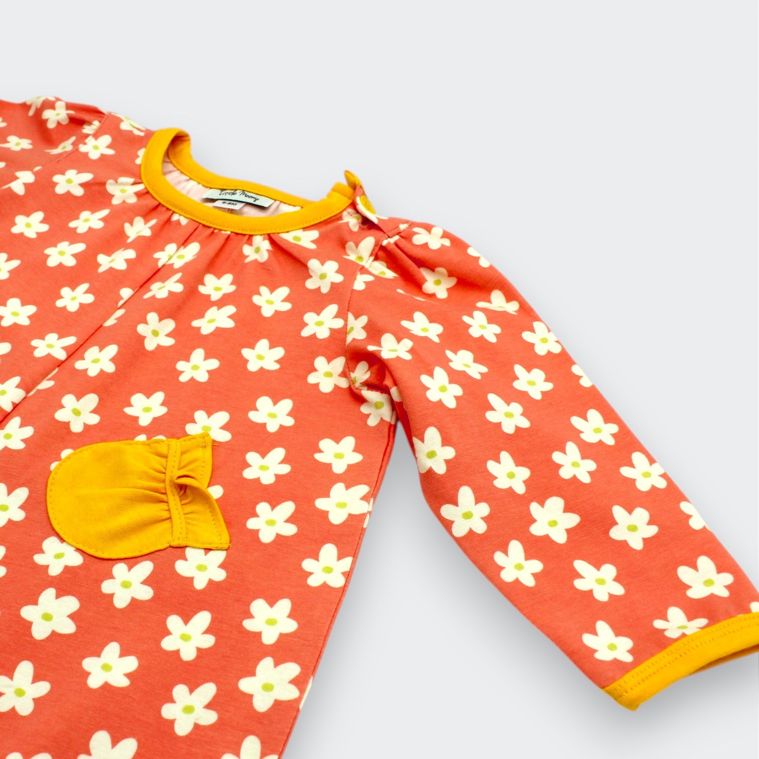 Little Moony Close-up of daisy floral baby romper showing marigold ruffled chest pocket and contrast ribbed cuff on coral interlock knit fabric