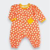 Little Moony Daisy floral baby romper in coral with cream daisy print, marigold ribbed trim at collar and cuffs, and ruffled chest pocket, full body view on white background
