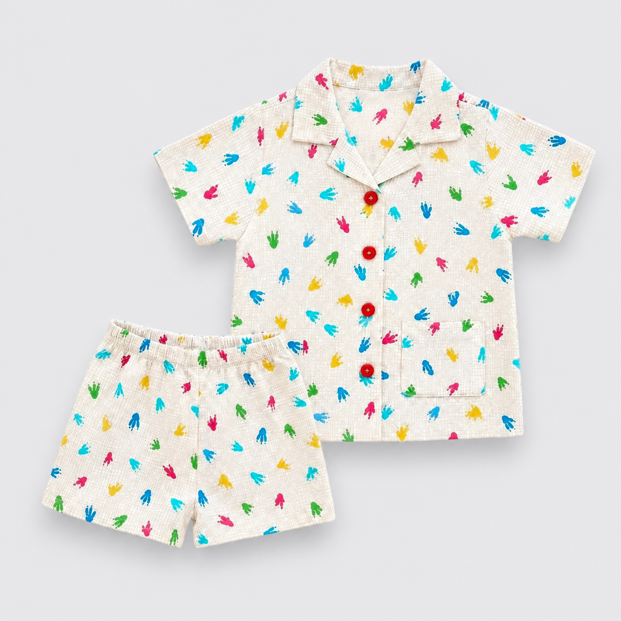 A Dinosaur set consisting of a short-sleeve button-up shirt and matching shorts in an off-white linen-like fabric, decorated with a colorful print of small handprints in blue, green, yellow, and pink. The shirt features red buttons.