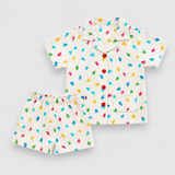 A Dinosaur set consisting of a short-sleeve button-up shirt and matching shorts in an off-white linen-like fabric, decorated with a colorful print of small handprints in blue, green, yellow, and pink. The shirt features red buttons.