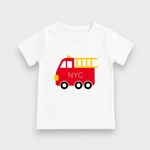 A white kids' short-sleeve t-shirt with a red fire truck graphic on the chest. The fire truck is decorated with a yellow ladder, yellow bumper, a yellow light, and the letters 'NYC' in white on the side.