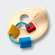 A wooden shape-sorting toy on a light gray background. Its pale wood base has a round handle opening and a recessed square slot, with yellow, red, and blue shapes threaded onto a teal cord.