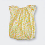 A sleeveless baby top with a ruffled neckline and an all-over small floral print in yellow, orange, and green on a light cream background, shown flat against a light gray background.