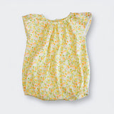 A sleeveless baby top with a ruffled neckline and an all-over small floral print in yellow, orange, and green on a light cream background, shown flat against a light gray background.