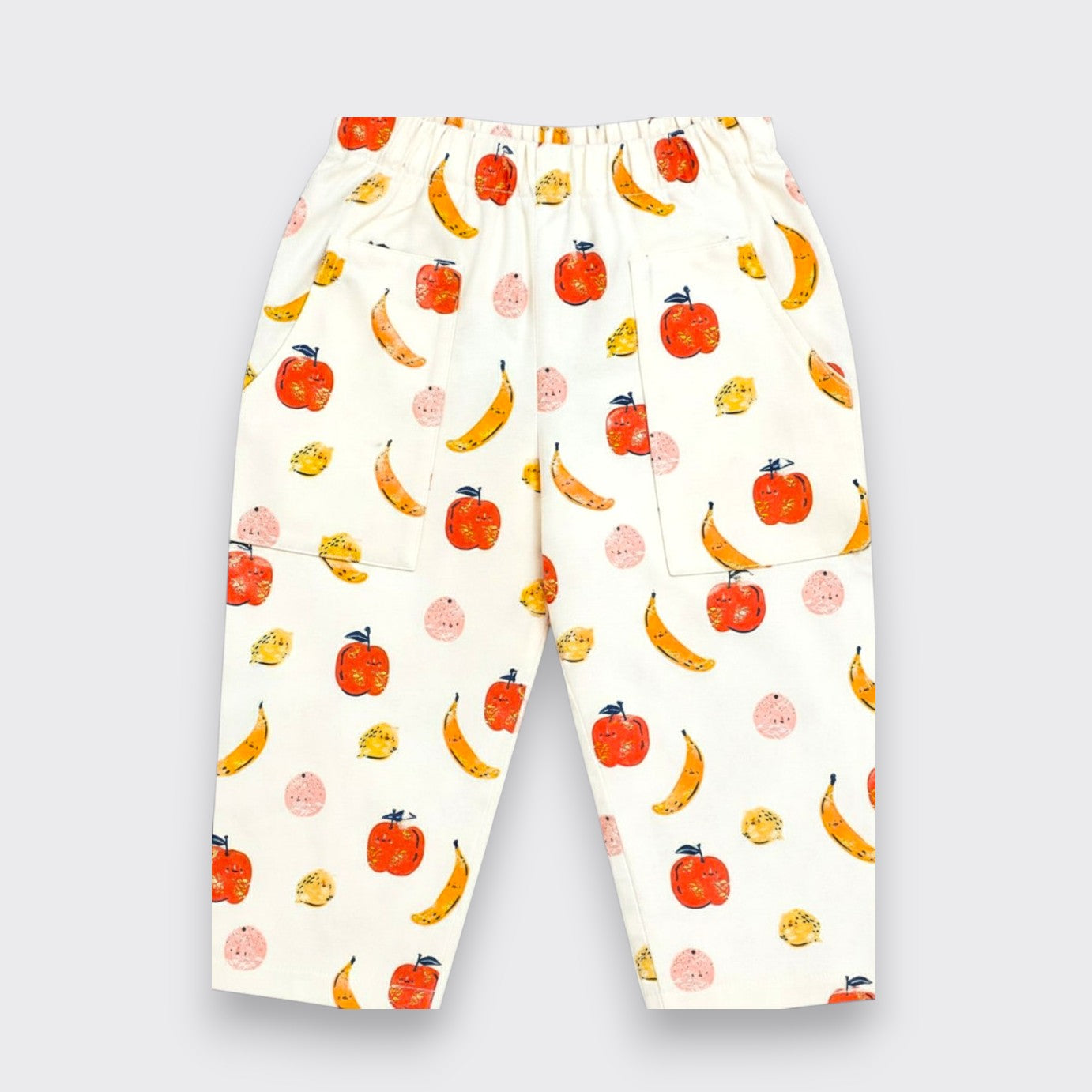 Little Moony White elastic-waist pants with an all-over watercolor fruit print of oranges, bananas, and pears, shown flat on a light gray background.