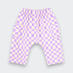 A pair of children's shorts featuring a lavender and cream checkerboard pattern, an elastic waistband, and side pockets, shown against a light gray background.