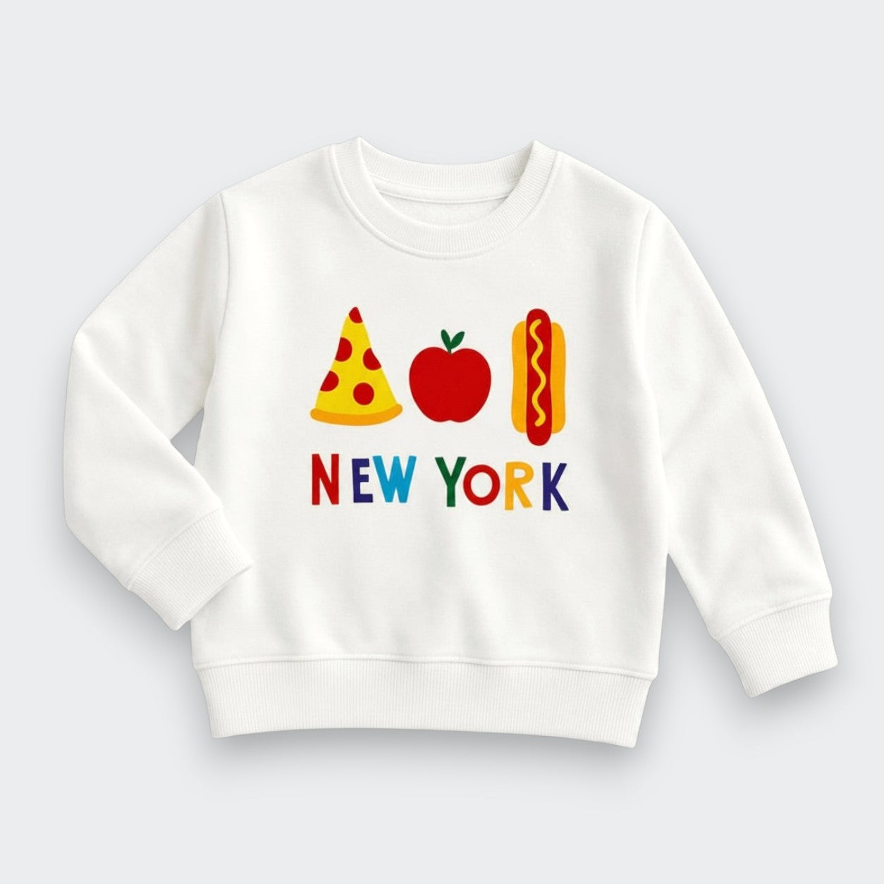 A white long-sleeve crewneck sweatshirt featuring a colorful graphic of a pizza slice, an apple, a hot dog, and the text 'NEW YORK' in multicolored letters on the front, displayed against a light gray background.