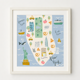 Framed New York City map art print featuring illustrated landmarks, taxis, pizza slices, and river sections on a light blue background, shown in a white frame against a white wall.