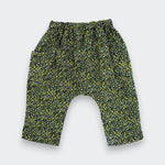 A pair of toddler's harem-style pants with an elastic waistband and a dense yellow and green floral print on a black background, shown flat on a light gray background.