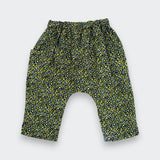 A pair of toddler's harem-style pants with an elastic waistband and a dense yellow and green floral print on a black background, shown flat on a light gray background.