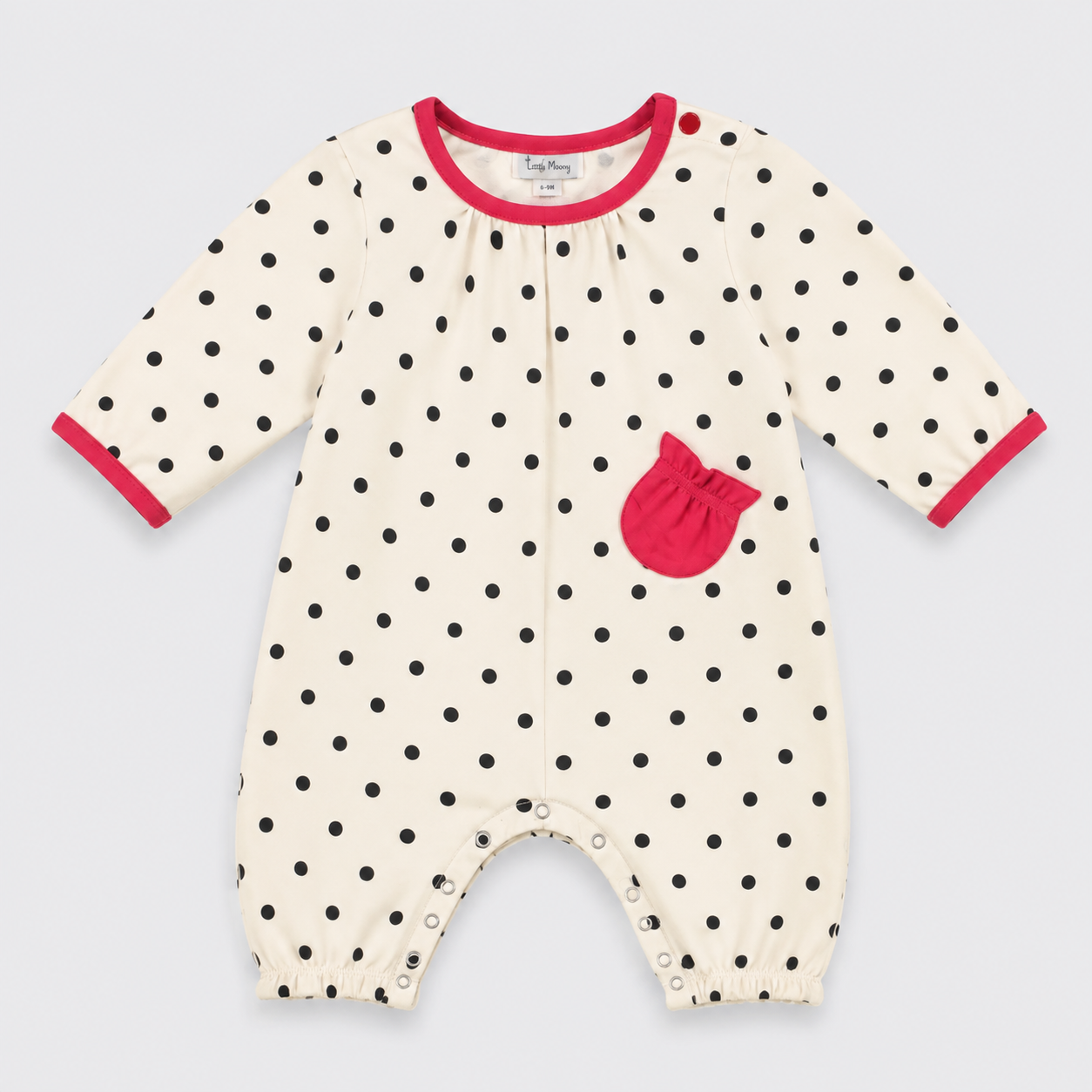 A baby long-sleeve footless romper in cream with black polka dots, featuring a bright pink pocket and pink trim on the collar and cuffs, shown on a light gray background.