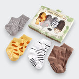 Four pairs of safari-themed baby socks displayed beside their “Sock Safari” gift box on a light gray background. The socks are gray with white spots, yellow with brown giraffe-like patches, white with black zebra stripes, and brown with narrow stripes.