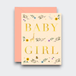 A cream greeting card reading “BABY GIRL” in large gold letters, decorated with delicate flowers, leafy sprigs, and tiny animal illustrations. A peach-pink envelope sits behind it.