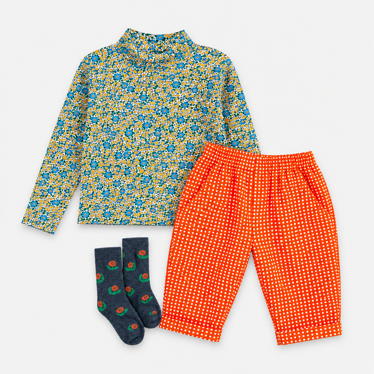 A children's three-piece outfit set featuring a long-sleeve mock neck shirt with a blue and yellow floral pattern, bright orange pants with white polka dots, and navy blue socks with a small red and green pattern, all laid flat on a white background.