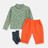 A children's three-piece outfit set featuring a long-sleeve mock neck shirt with a blue and yellow floral pattern, bright orange pants with white polka dots, and navy blue socks with a small red and green pattern, all laid flat on a white background.