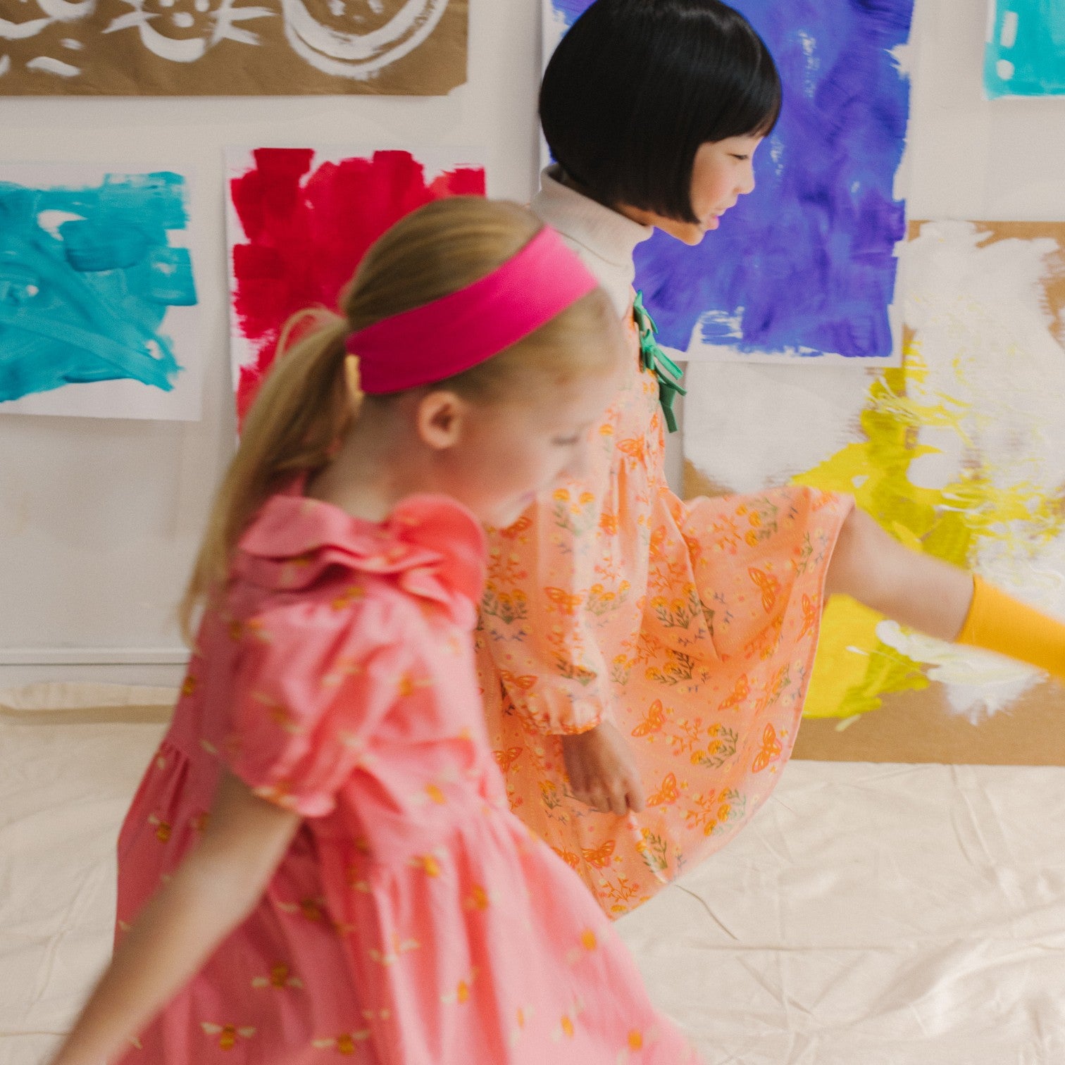 Two children in colorful Little Moony cotton butterfly and bee special occasion dresses standing in front of a wall with abstract paintings.