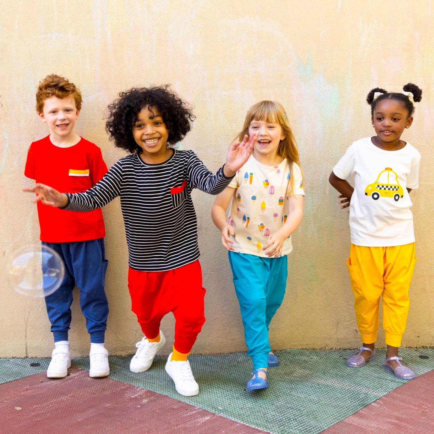 Four children standing together against a beige wall with colorful Little Moony cotton knit jogger pants. 