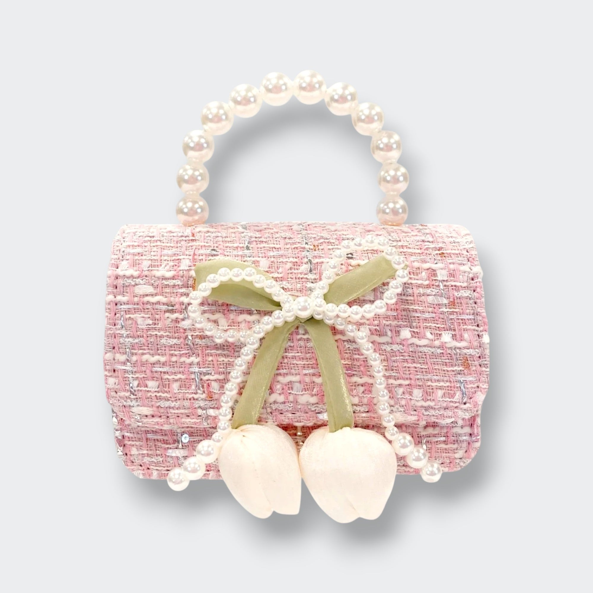 A small pink tweed purse with a rounded pearl-bead handle. A pearl-trimmed bow and two dangling white flower buds decorate the front, photographed against a light gray background.