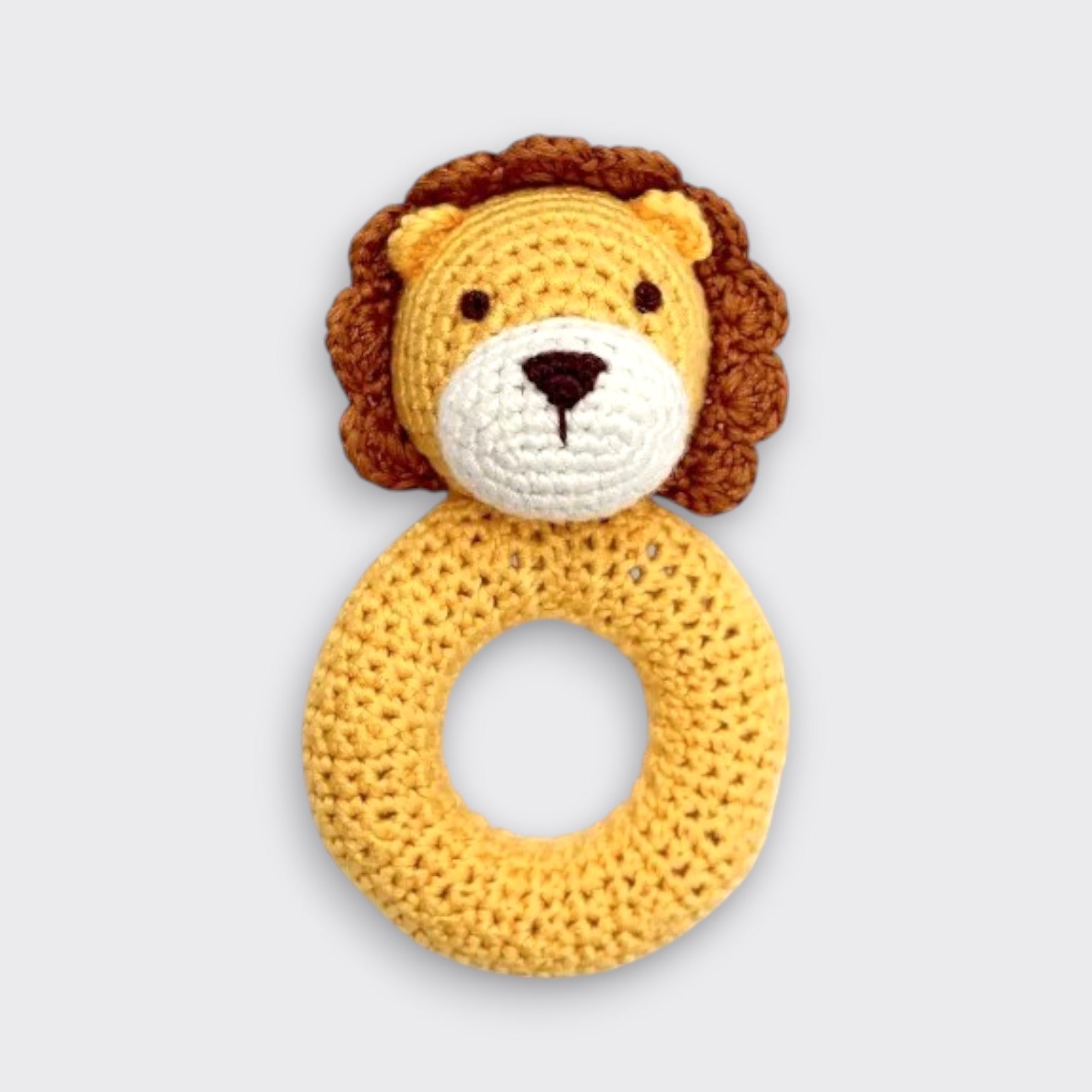 A crocheted lion baby rattle on a light gray background. Its yellow ring handle sits beneath a lion’s face with a brown mane, small round ears, a white muzzle, and a dark embroidered nose.