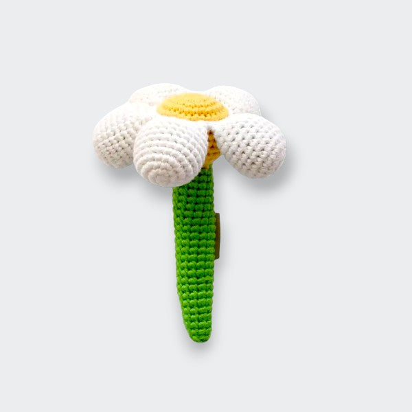 A crocheted flower baby rattle on a light gray background, with white petals, a yellow center, and a bright green stem that serves as the handle.
