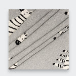 Close-up of a gray knit baby blanket folded in overlapping layers on a light gray background, showing the knit texture and parts of its black-and-white zebra pattern.
