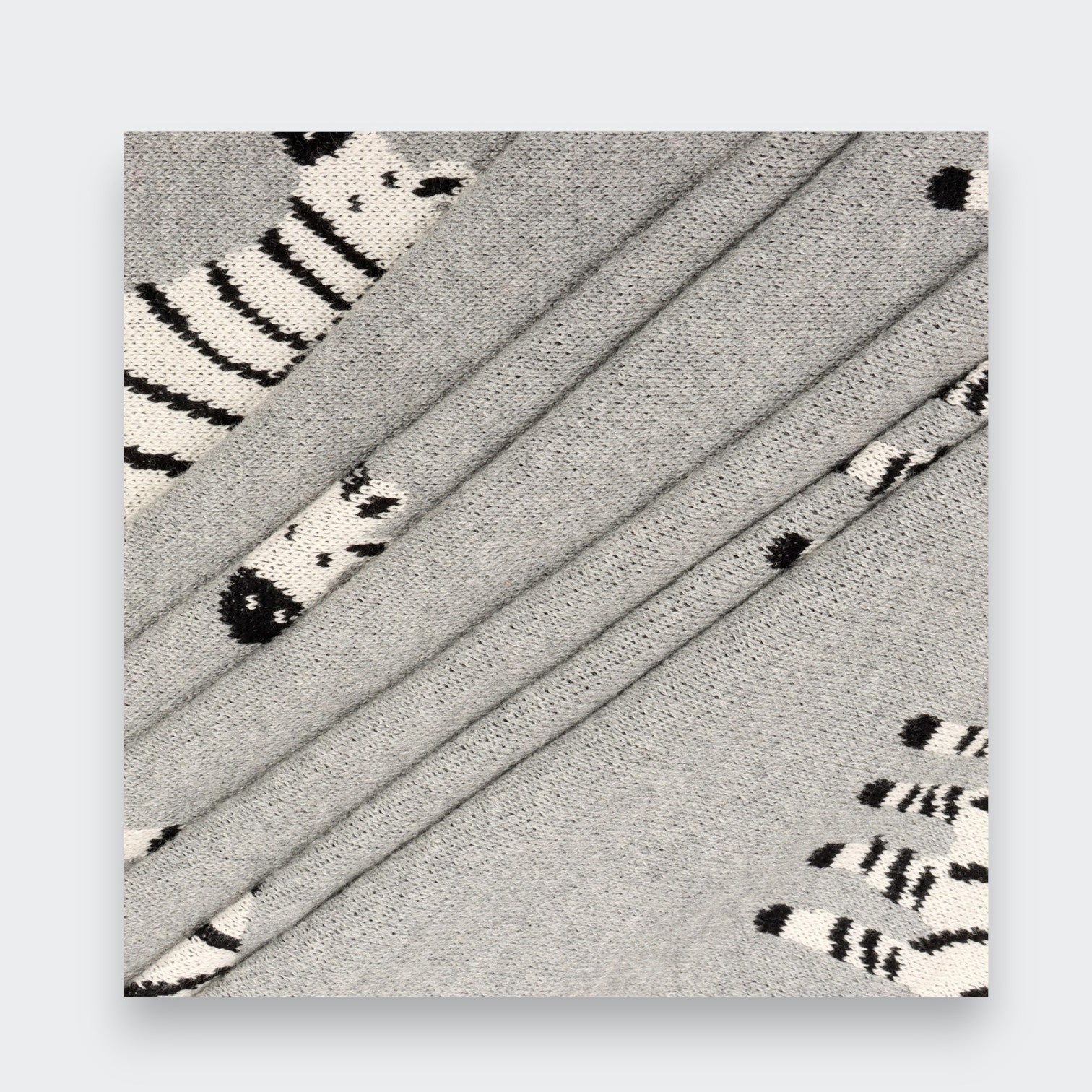 Close-up of a gray knit baby blanket folded in overlapping layers on a light gray background, showing the knit texture and parts of its black-and-white zebra pattern.