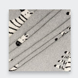 Close-up of a gray knit baby blanket folded in overlapping layers on a light gray background, showing the knit texture and parts of its black-and-white zebra pattern.