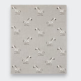 A gray knit baby blanket spread flat on a light gray background, showing an allover pattern of small black-and-white zebras arranged in rows.