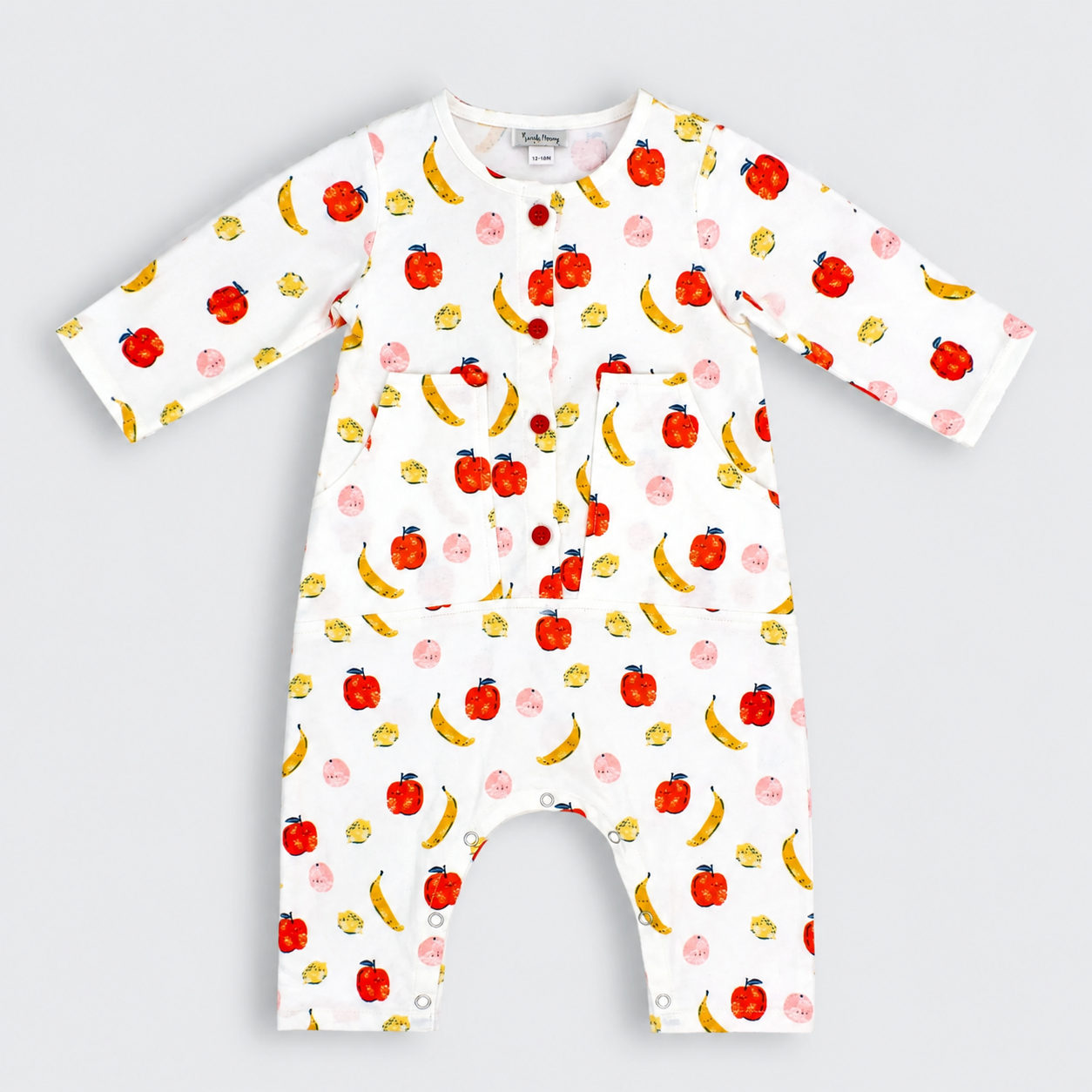 A white long-sleeve baby romper with an all-over fruit print of red apples, yellow bananas, and pink pears, featuring a snap-button front and chest pockets, shown on a light gray background.
