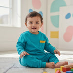 Child wearing a blue outfit with a yellow pocket, sitting on the floor with colorful blocks.