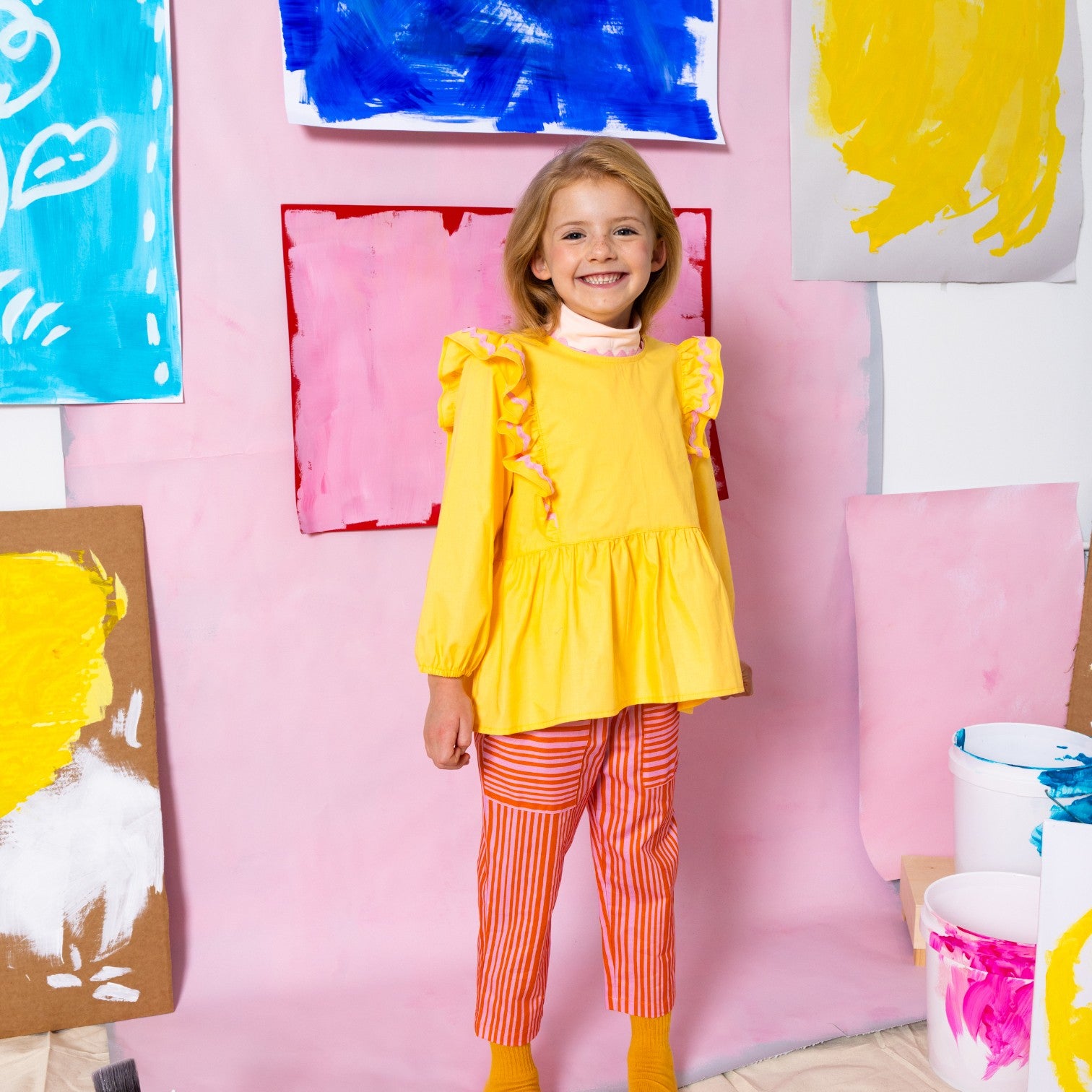 Young girl in Little Moony cherry red and pink stripe patch pocket pants with colorful background
