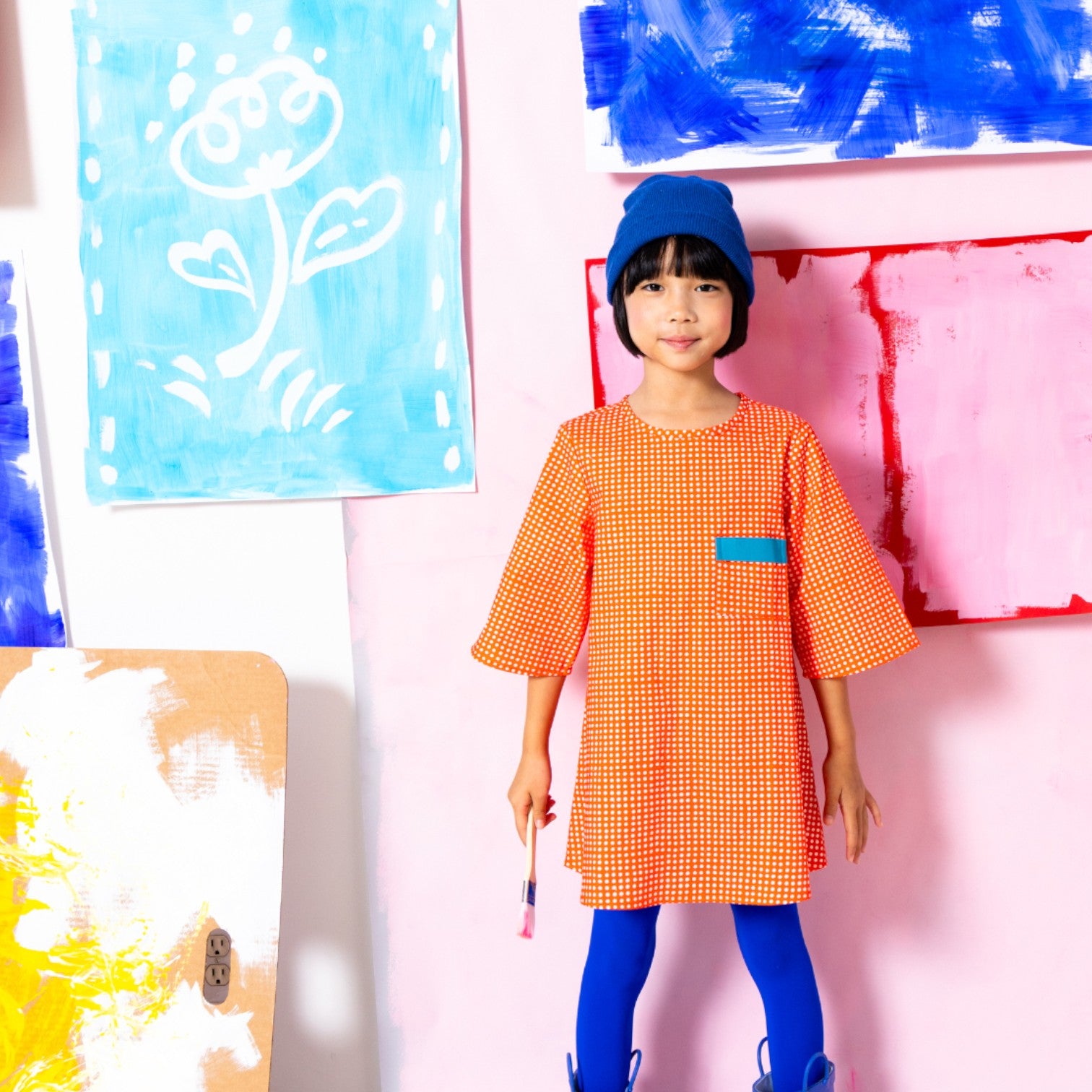 Girl wearing Little Moony cherry red polka dot pocket dress with teal contrast pocket and bell sleeves