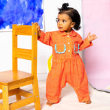 Baby Girl in Little Moony Cherry Dot Cotton Ruffle Pocket Romper beside a chair