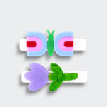 Two white hair clips featuring a blue and pink butterfly and a glittery purple tulip with green leaves on a light gray background.