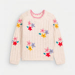 Cream knit sweater with colorful floral embellishments, pink neckline trim, and ribbed cuffs, shown from the front on a light gray background.