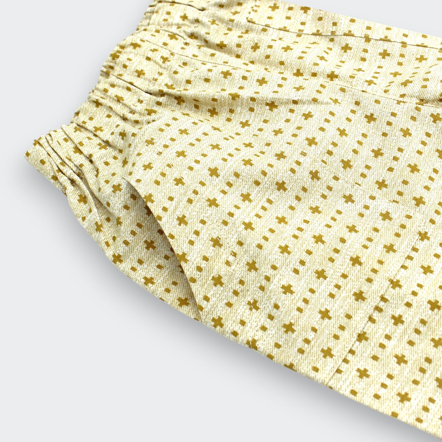 Close up detail of Little Moony cross-stitch print cotton baby and toddler pants showing cream base, brown cross motifs and patch pockets
