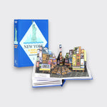 New York: A Pop-Up Book by Dominique Ehrhard, shown open to a Times Square pop-up scene with billboards and yellow taxis, beside its blue cover on a light gray background.