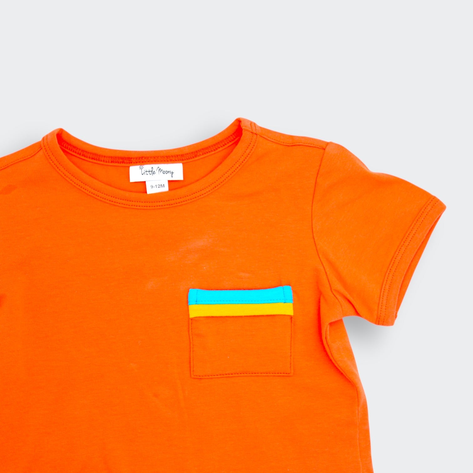 Close up detail of Little Moony orange colorblock pocket tee showing teal and yellow striped patch pocket