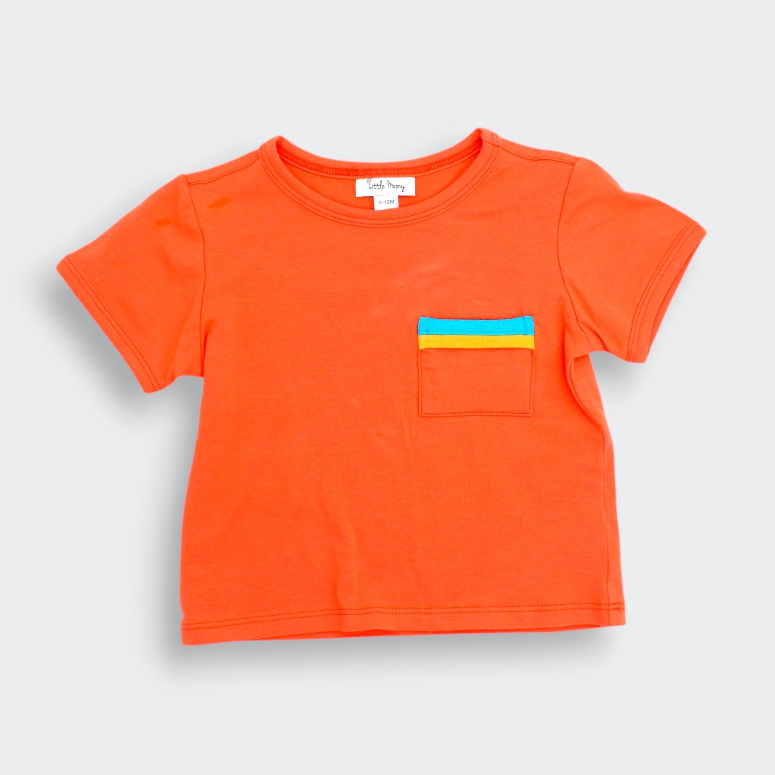Little Moony orange colorblock pocket tee for baby and toddler with teal and yellow patch pocket flat lay view
