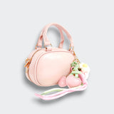 Angled view of a pink bowler purse with a zip closure, heart and floral charms, and trailing pastel ribbons on a light gray background.
