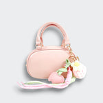 Front view of a pink bowler purse with twin handles, pink heart charms, a white flower charm, and pastel ribbons on a light gray background.