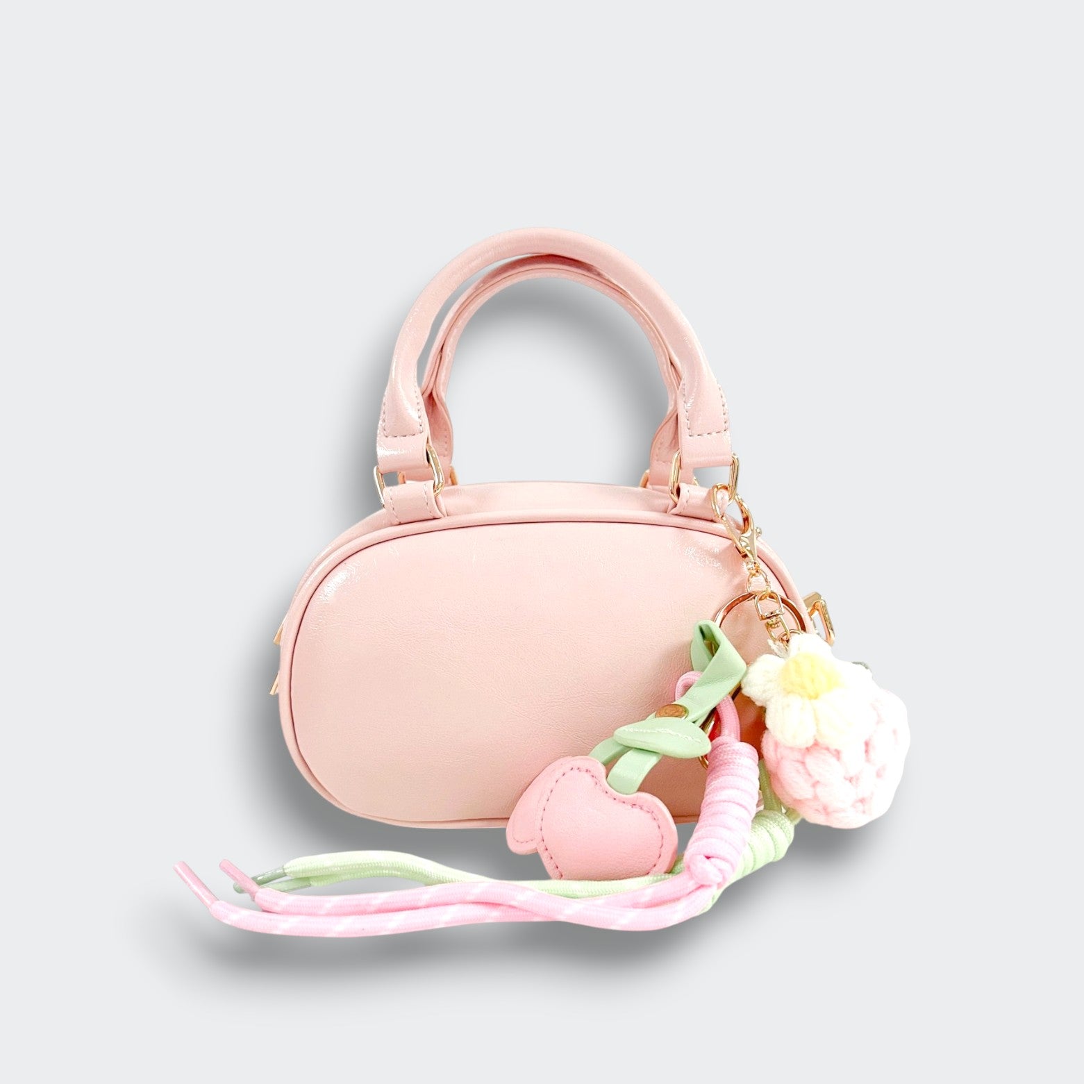 Front view of a pink bowler purse with twin handles, pink heart charms, a white flower charm, and pastel ribbons on a light gray background.