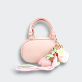 Front view of a pink bowler purse with twin handles, pink heart charms, a white flower charm, and pastel ribbons on a light gray background.