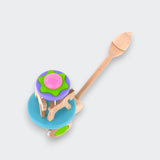 Top view of a wooden carousel push toy with a pink, green, and purple canopy, wooden horses, and a turquoise base on a light gray background.