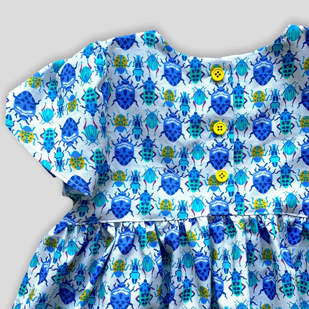 Blue Bug Dress with Tulip Sleeves and Bow for Babies and Kids. Detail view of yellow buttons on the back side.